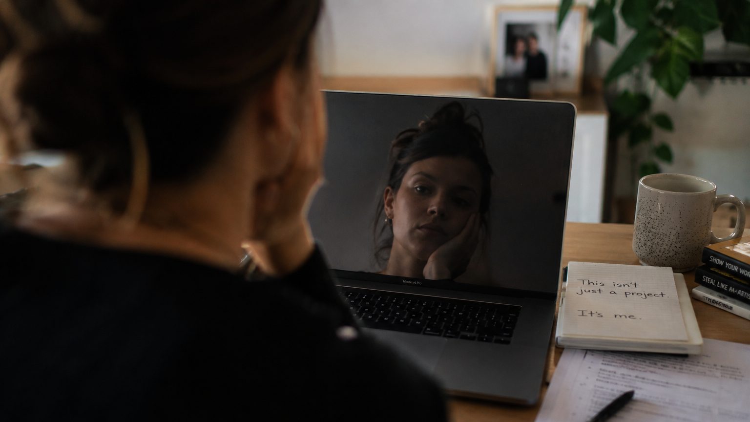 A freelancer or solo founder looking at their reflection in a laptop screen, suggesting the emotional weight of personal identity being tied to the work they are about to release.